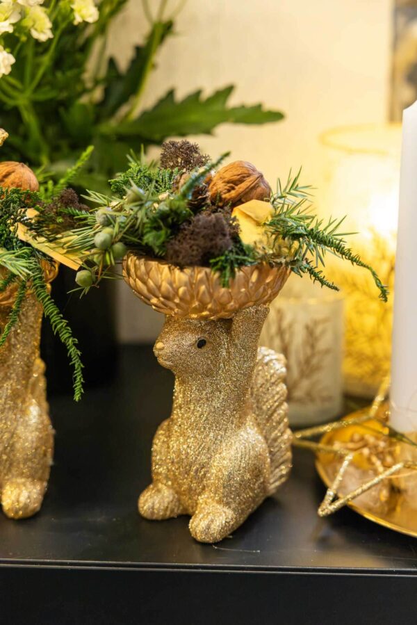 Goldenes Eichhörnchen hält eine Nussschale mit Grün als weihnachtliche Dekoration bei Rose & Co